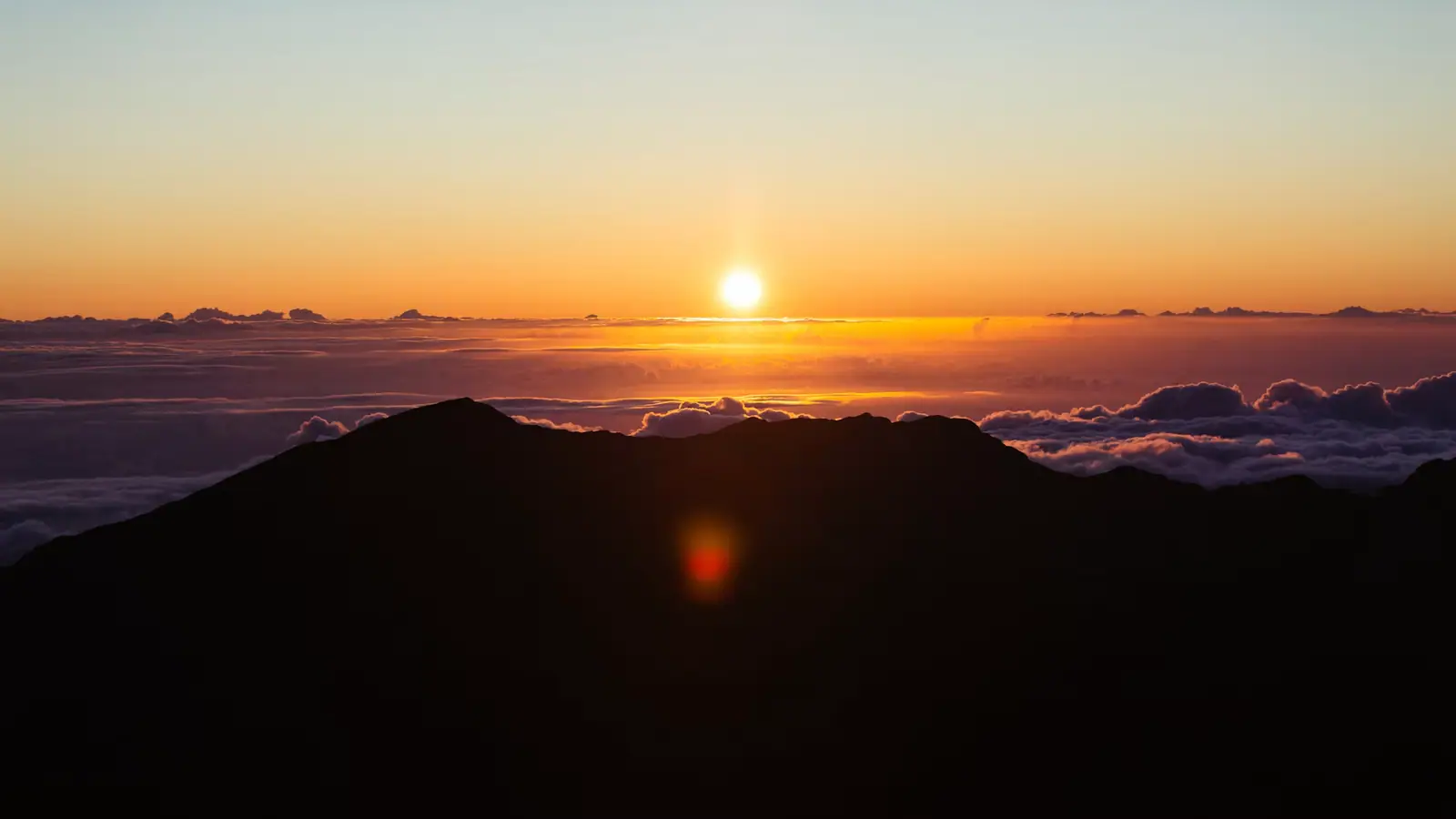 A sea of cloud lying below a bare volcanic summit ridge at first light