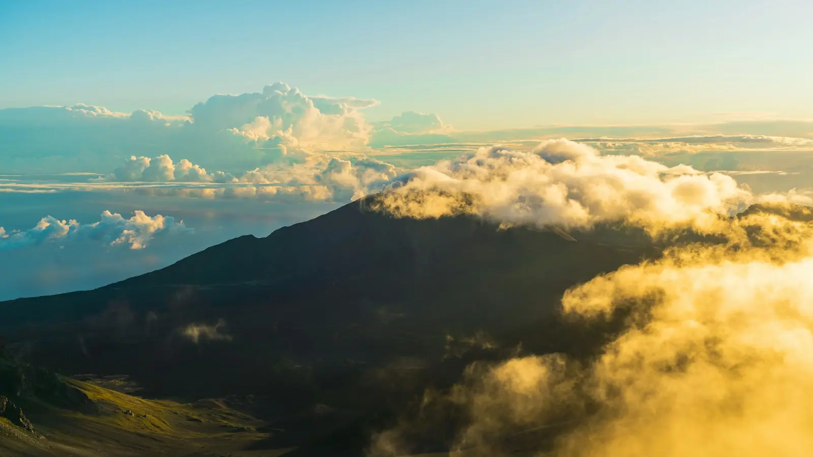 Dawn light over the cinder cones and ridgelines of the Haleakalā summit depression on Maui, above a layer of cloud