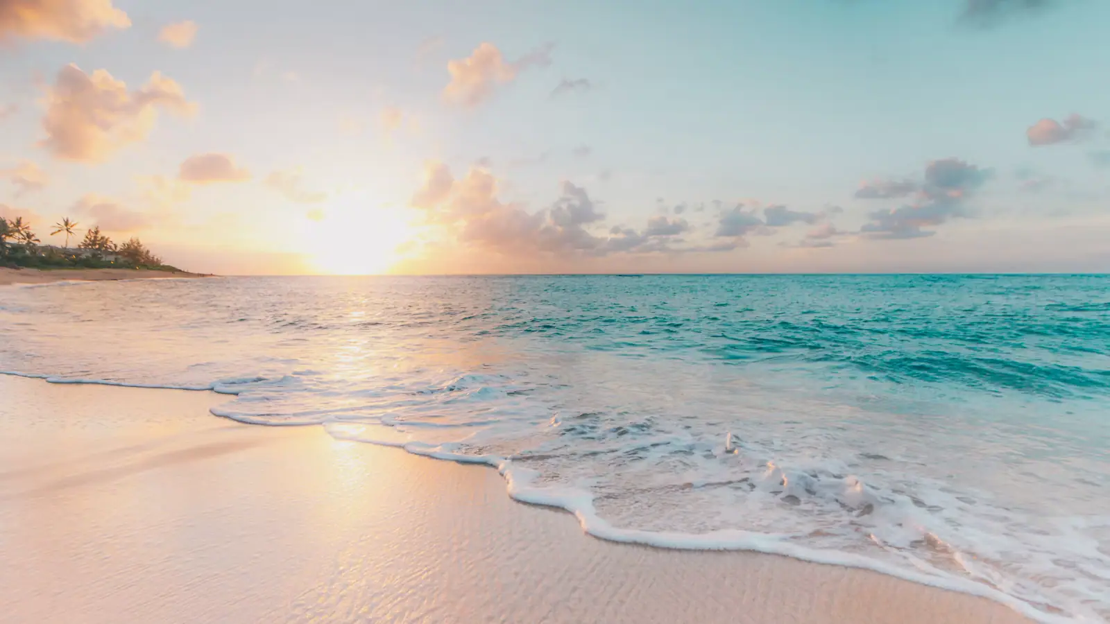 Clear shallow water breaking gently onto pale sand under a bright sky