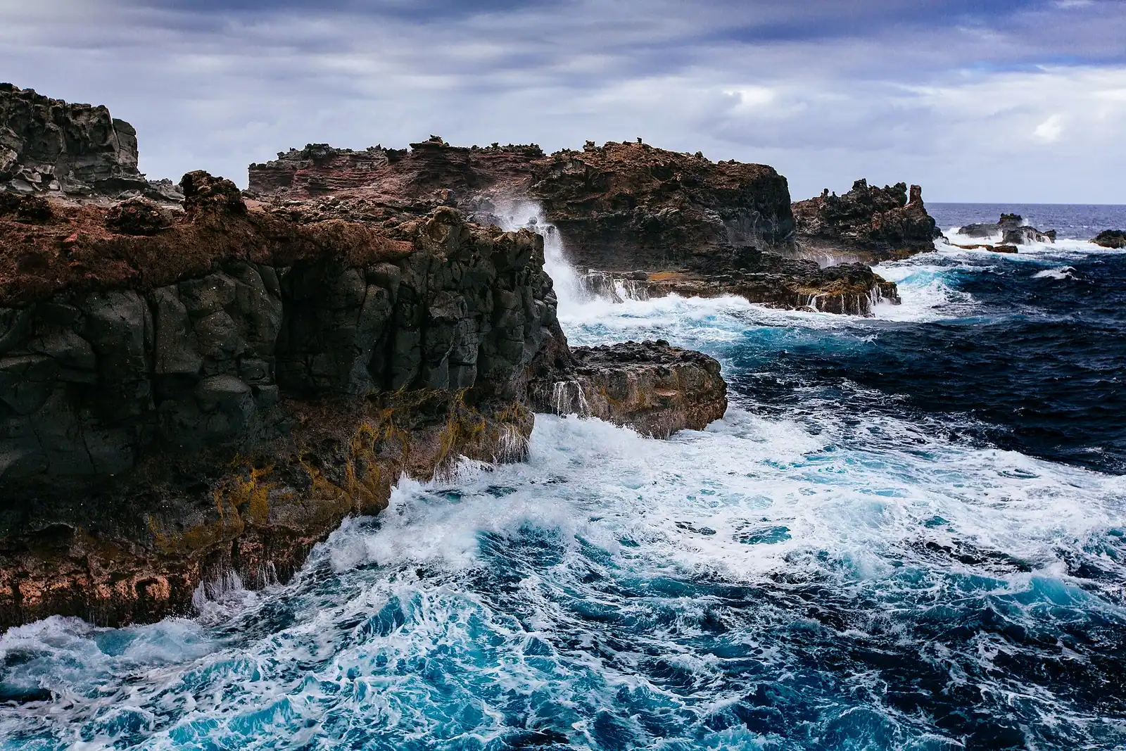 A plume of seawater bursting upward from a hole in dark coastal rock