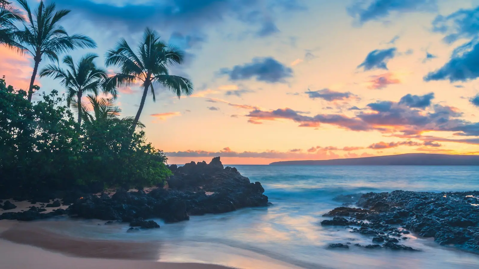 Late afternoon light on the coastline of Maui with volcanic rock shelves in the foreground and the West Maui Mountains behind