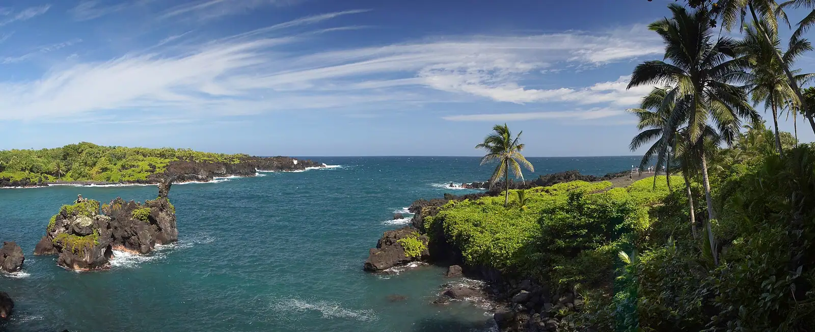 Dark volcanic sand and black rock at the edge of a small ocean cove